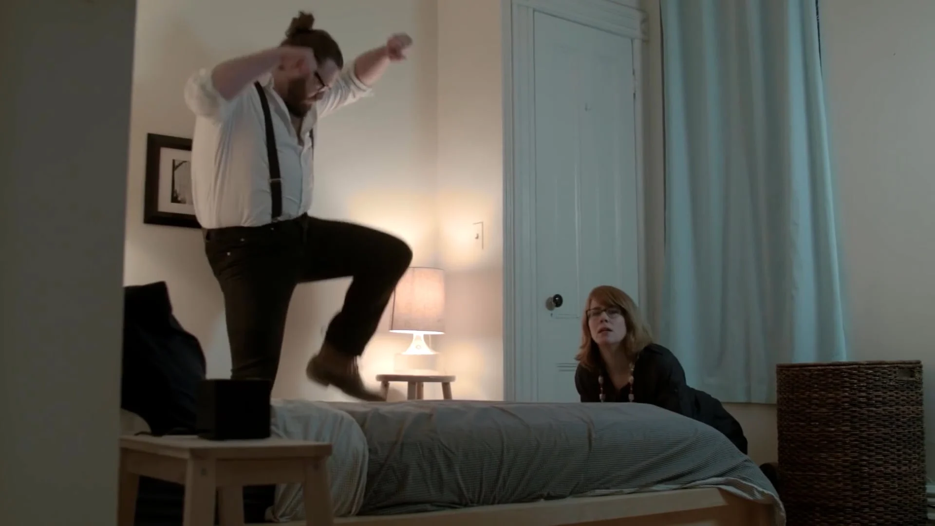 A man stomping on a bed in an apartment